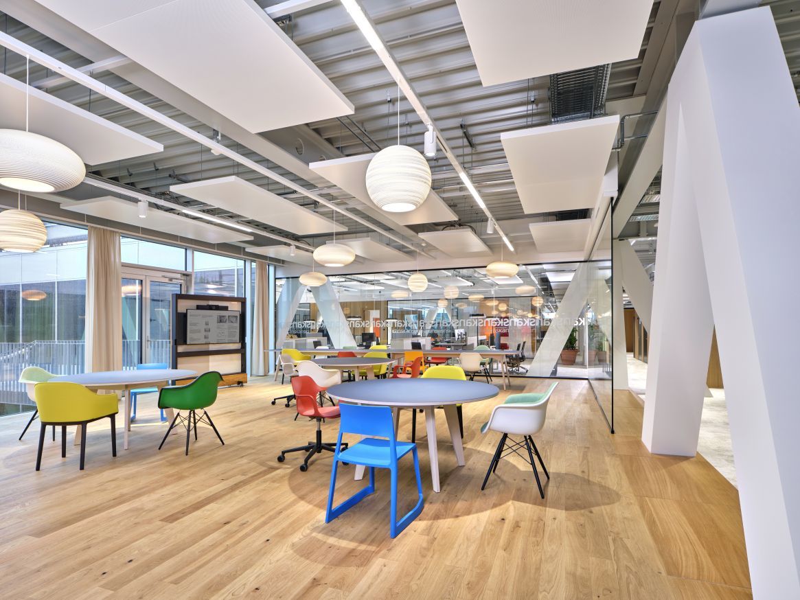 Helles Büro mit farbenfrohen Stühlen, darunter ein Vitra Hal Drehstuhl, an runden Tischen.