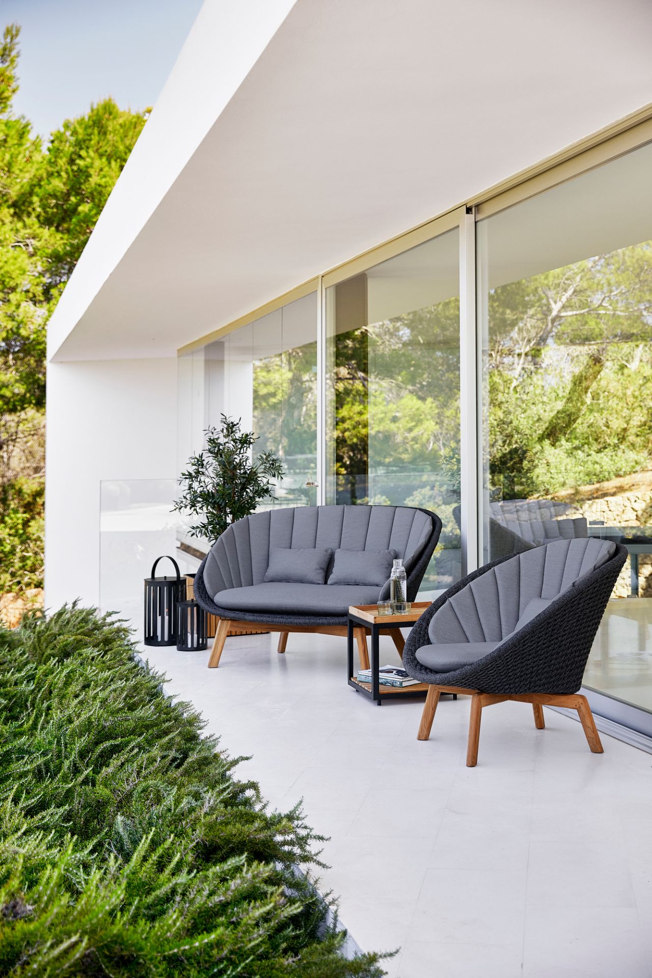 Cane-Line Peacock Outdoor Lounge Set: 2-Sitzer Sofa und Sessel auf einer Terrasse. Graue Polster.