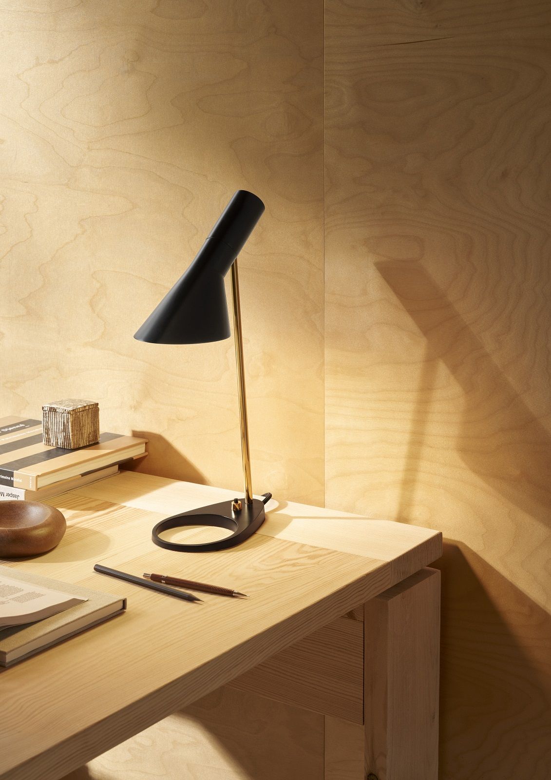 Schwarze AJ Mini Tischleuchte von Louis Poulsen auf einem Schreibtisch mit Büchern und Stiften.