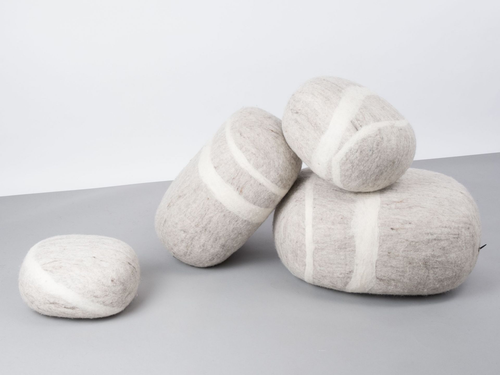 Grauer Filz Kieselstein Hocker von myfelt, Béla L, mit weißen Streifen, dekorativ und bequem.