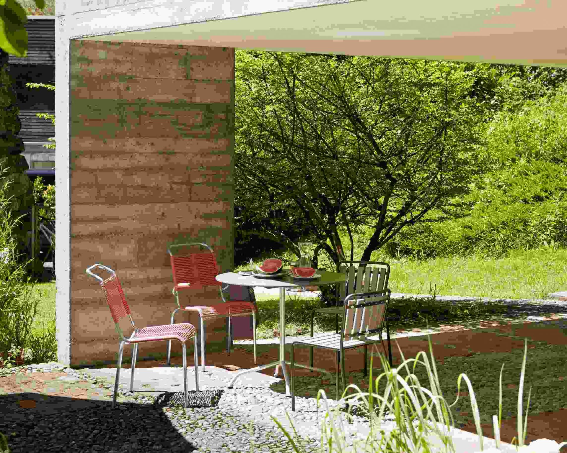Altorfer Sessel Outdoor Embru in Graphitschwarz an Gartentisch mit Wassermelone, stilvolle Gartenmöbel für Terrasse.