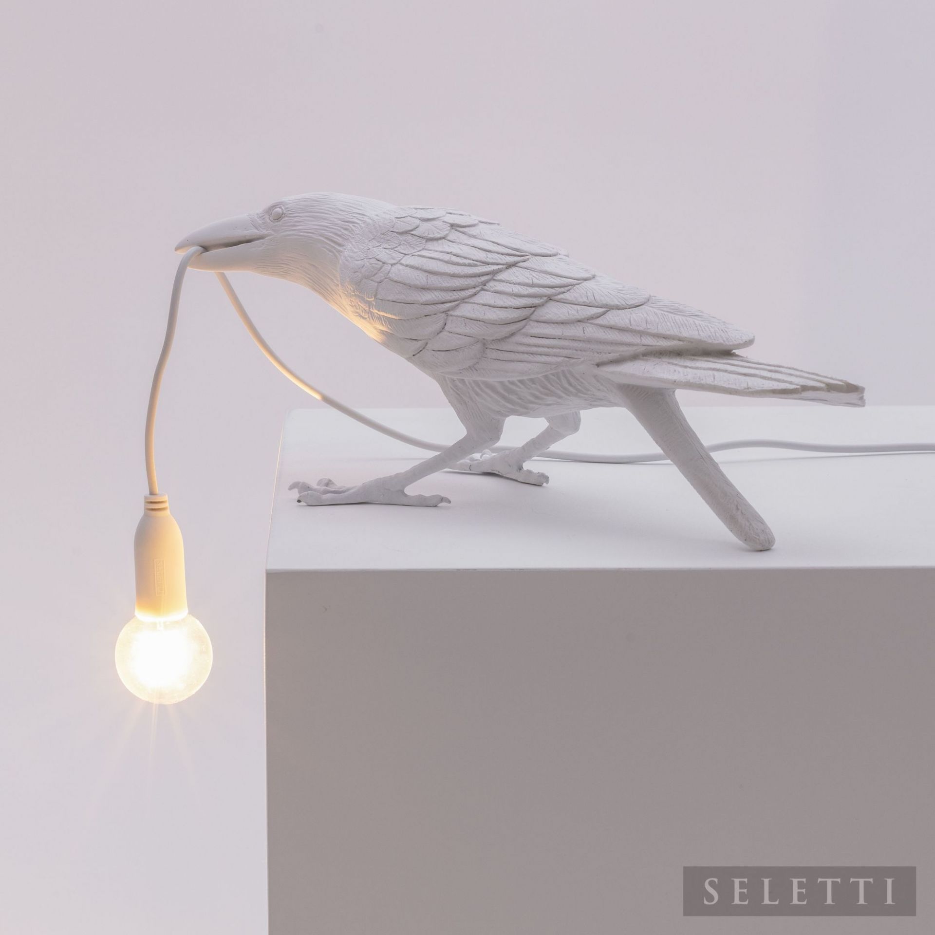 Weiße Seletti Bird Lamp "Playing" als Designleuchte, Vogel hält Glühbirne im Schnabel.