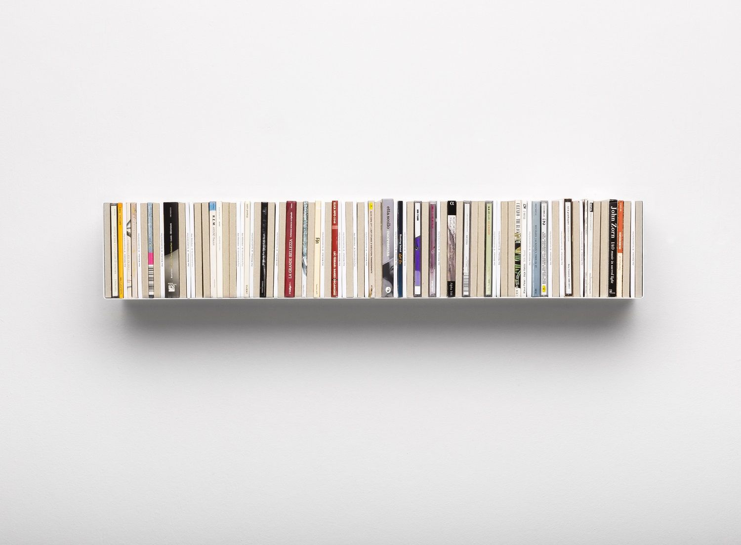 Silbernes CD-Regal Linea1 von Müller Möbelwerkstätten, gefüllt mit CDs, an einer weißen Wand. Minimalistisches Design für Musikliebhaber.
