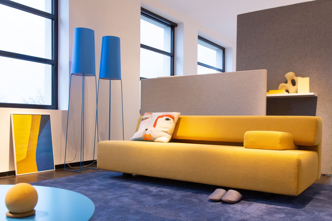 Gelbes Cosma Schlafsofa mit Kissen in modernem Wohnzimmer mit blauen Lampen und Teppich.