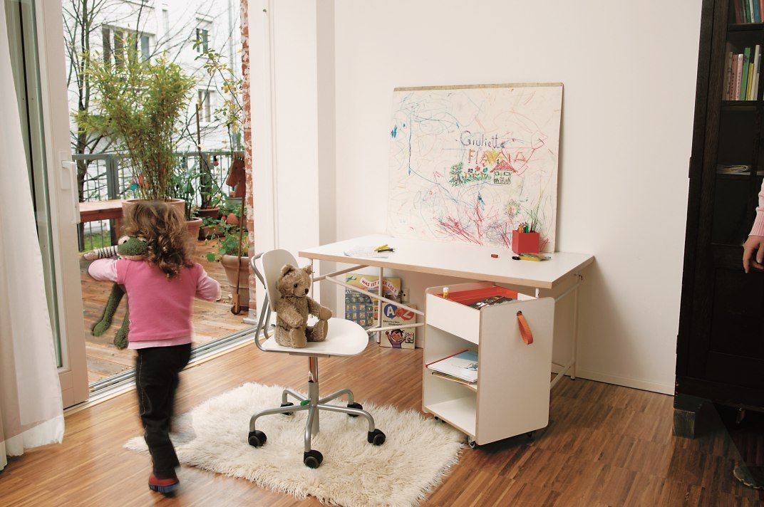 Kinderzimmer mit Kind, Schreibtisch, Stuhl und Richard Lampert Container Fixx zur Aufbewahrung von Spielsachen.