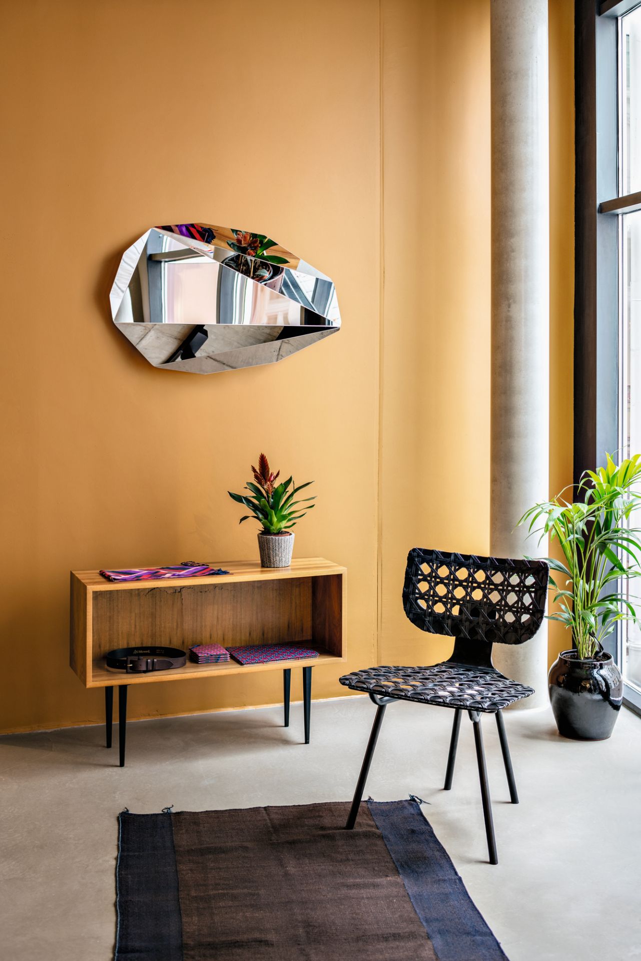 Wohnraum mit Piega Mirror Wandspiegel von Classicon, Sideboard, Stuhl und Zimmerpflanzen.