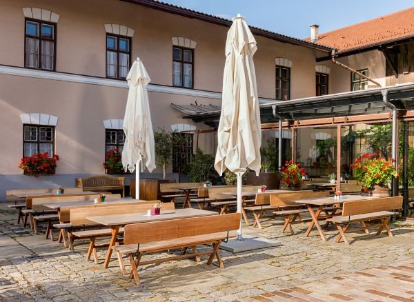 Weishäupl Sonnenschirme: Außenbereich eines Restaurants mit Holztischen, Bänken und weißen, geschlossenen Teleskopschirmen für Sonnenschutz.