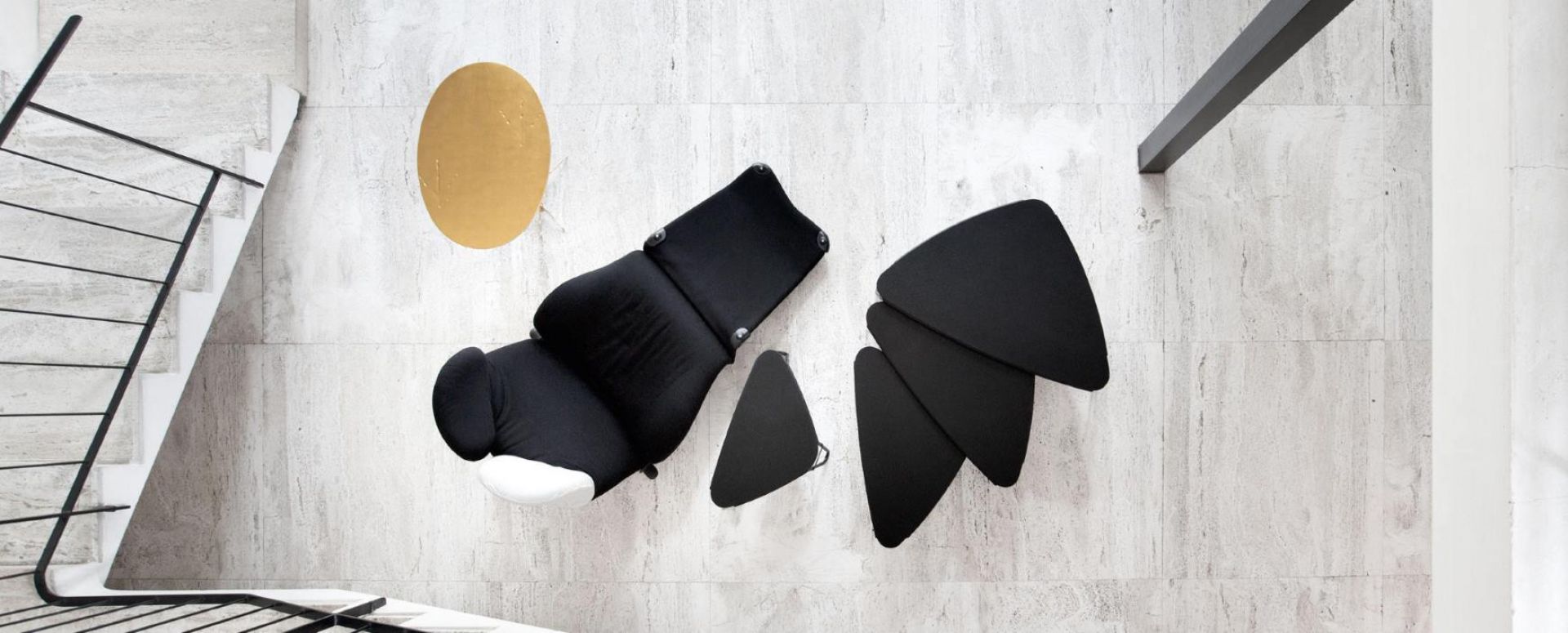 Draufsicht: Schwarzer Cassina Wink Sessel mit Fußhocker auf hellem Steinboden, modernes Möbeldesign.