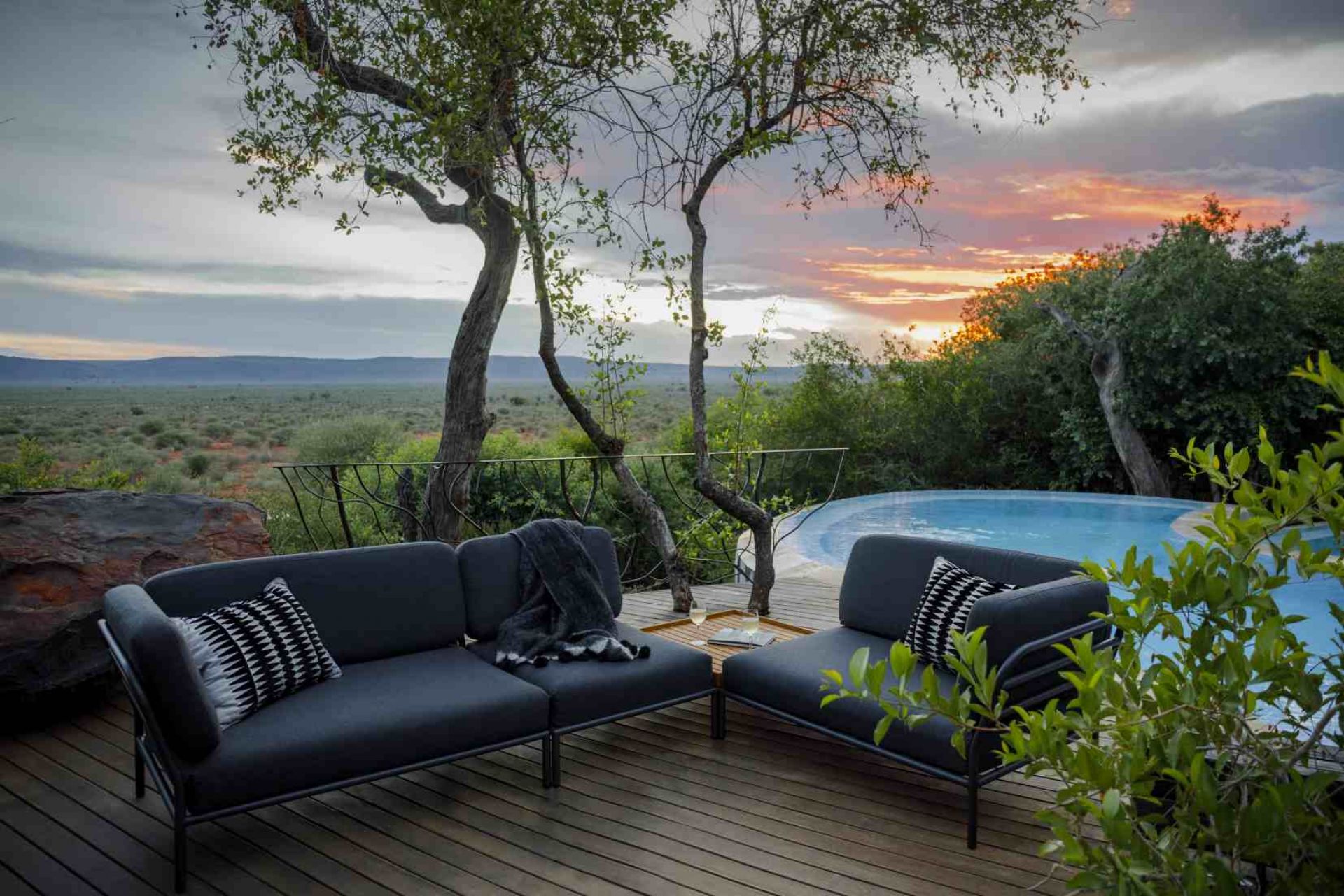 Level Sofa Outdoor Houe: Graues Gartensofa mit Kissen und Decke auf Holzterrasse am Pool.