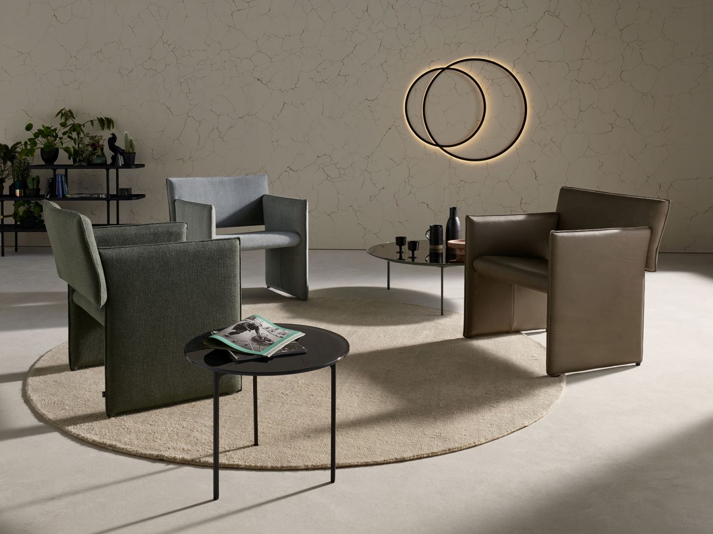 Wohnzimmer mit drei Noto Sesseln von Cor in Grau, Grün und Braun auf Teppich.