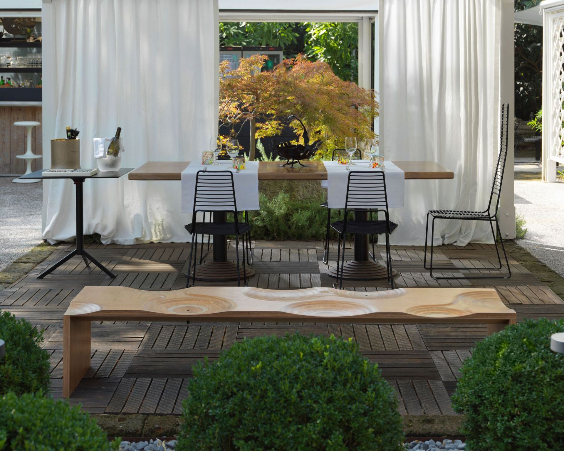 Casamania Horm Ripples Outdoor Bank aus hellem Holz mit wellenförmigem Muster im Garten.