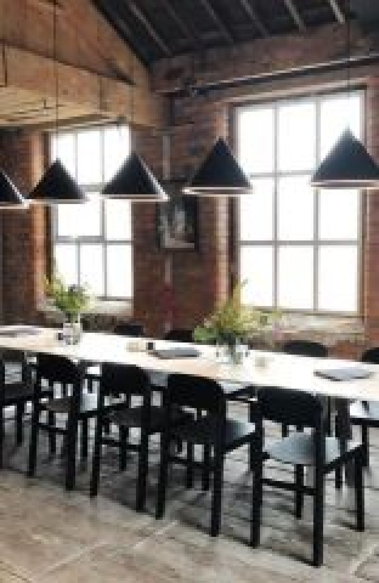 Schwarze Annular Pendelleuchten von Woud über einem langen Esstisch in einem Loft. Designlampe.