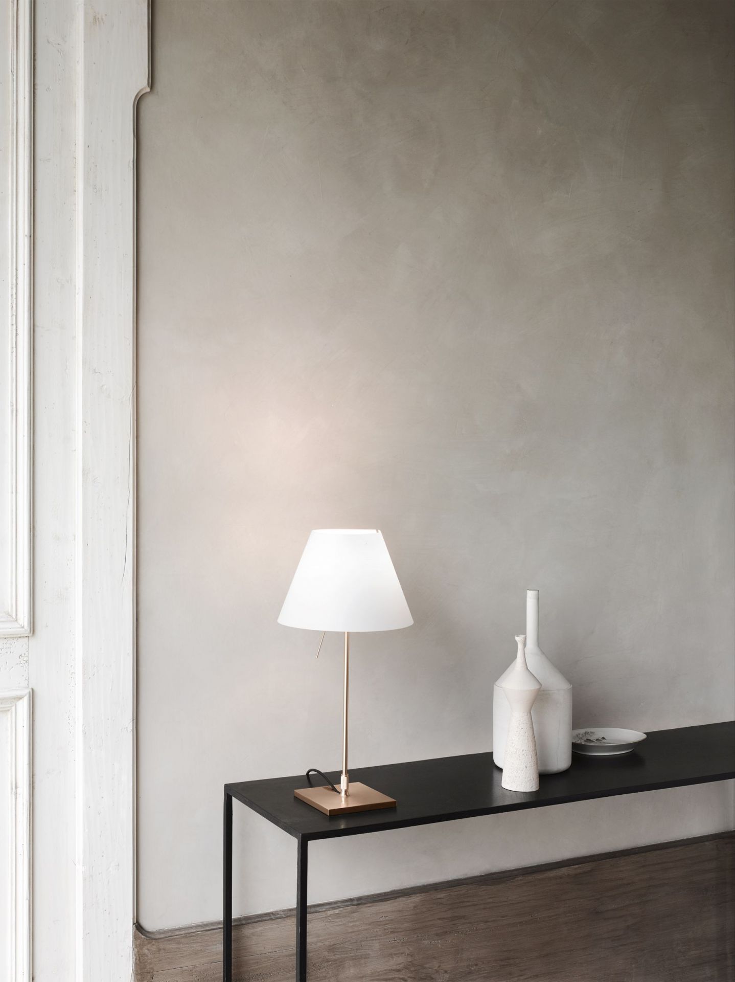 D13 Costanzina LED Tischleuchte von Luceplan mit Aluminiumgestell und weißem Lampenschirm auf schwarzem Tisch.