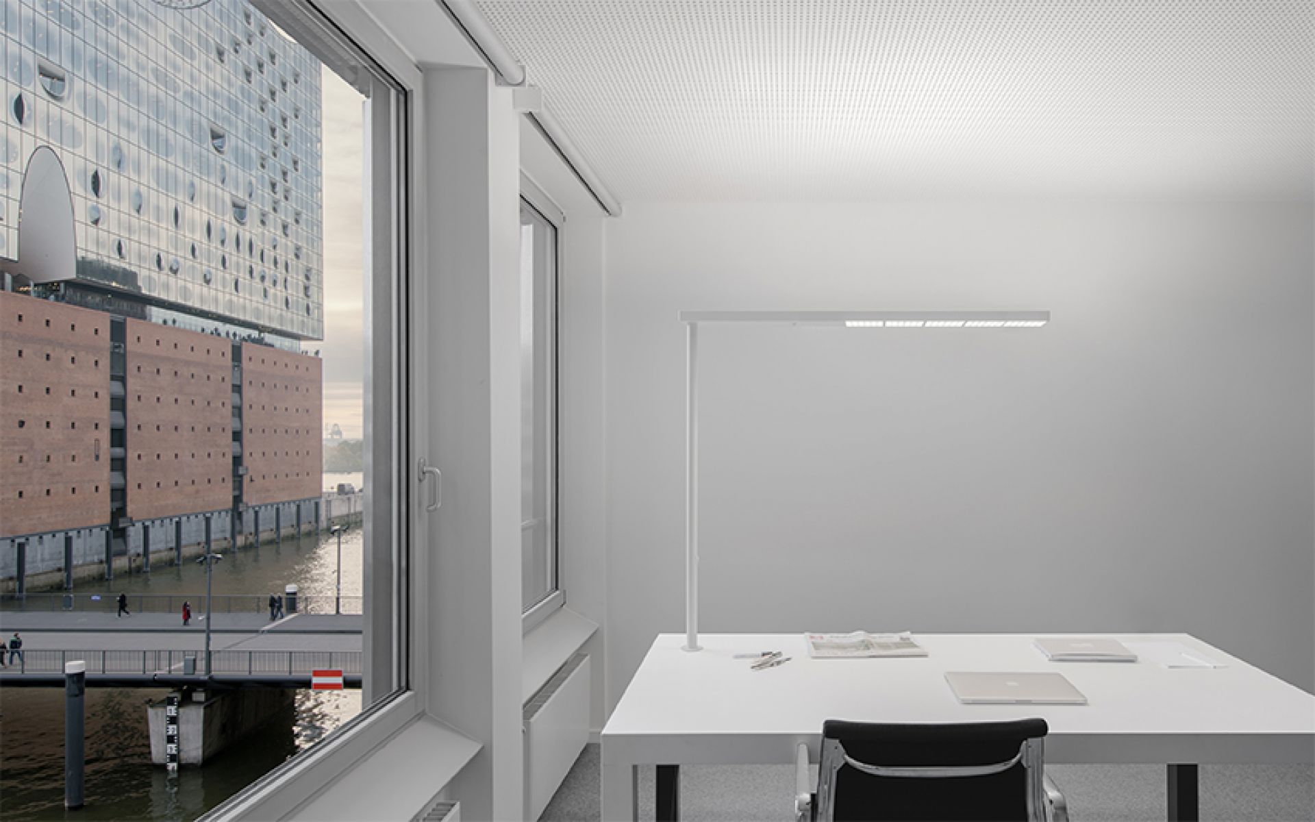 Moderne XT-A Plus Stehleuchte in Grau über einem weißen Schreibtisch mit Laptop und Büromaterial.