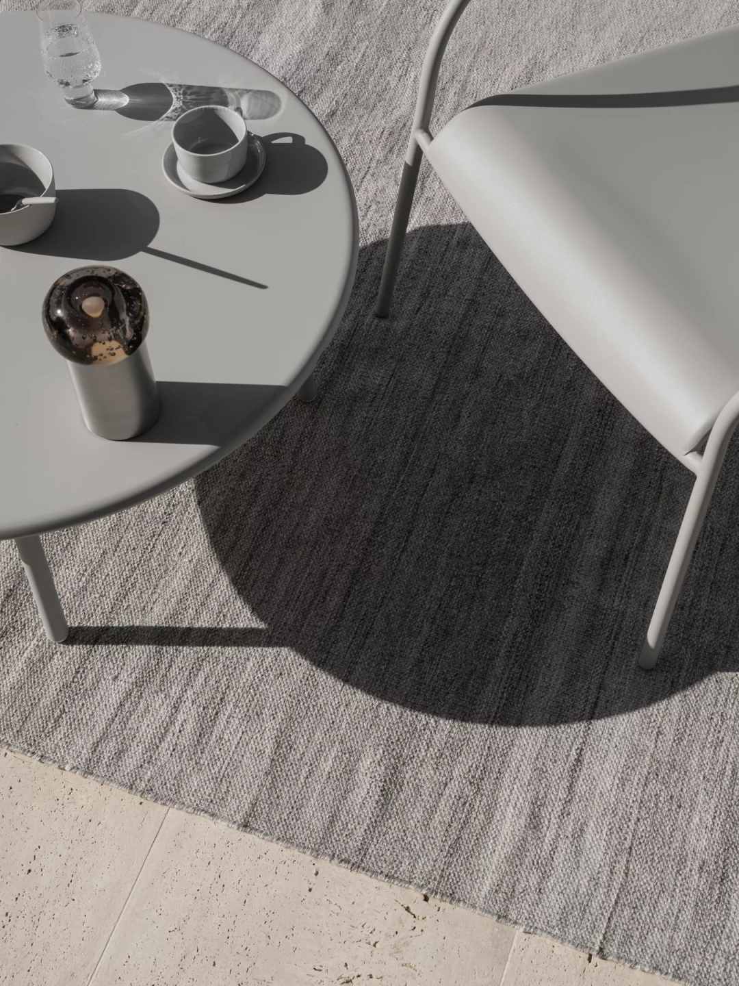 Detailaufnahme des Blomus Kiva Rug Outdoor Teppichs (B 140 cm) in Grau, mit Tisch und Stuhl.