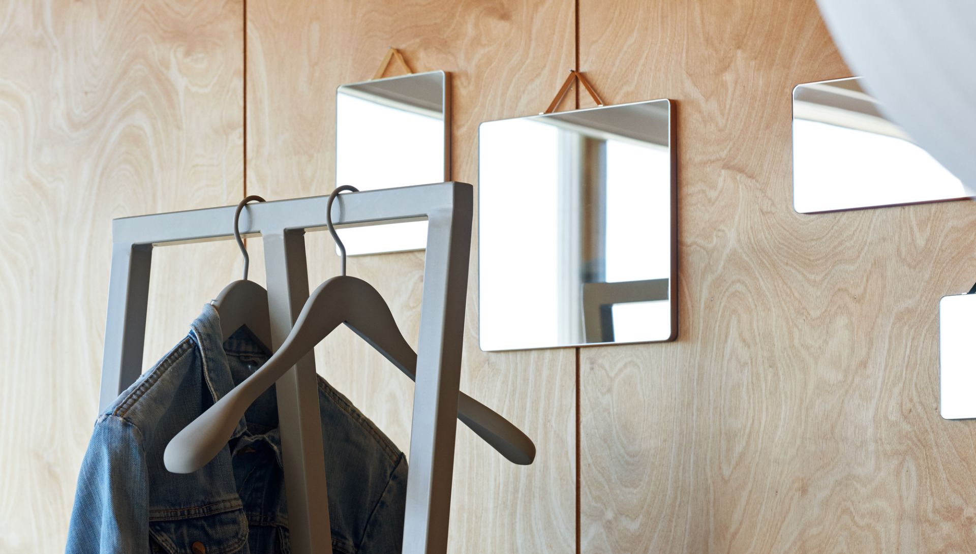 Hay Soft Coat Hanger: Graue Kleiderbügel an Garderobe mit Jacke vor Holzpaneel und Spiegeln.