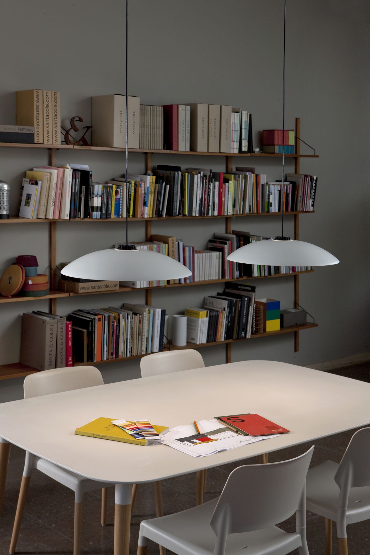 Heller Belloch Esstisch von Santa & Cole mit Stühlen und Pendelleuchten vor Bücherregal.