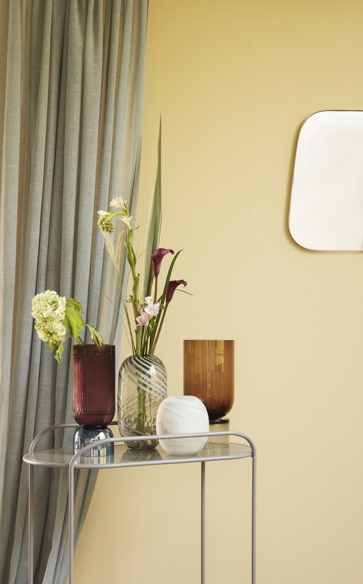 Verschiedene dekorative Vasen, darunter eine grün-weiße Glasvase von Hübsch Interior, mit Blumen auf einem Beistelltisch.