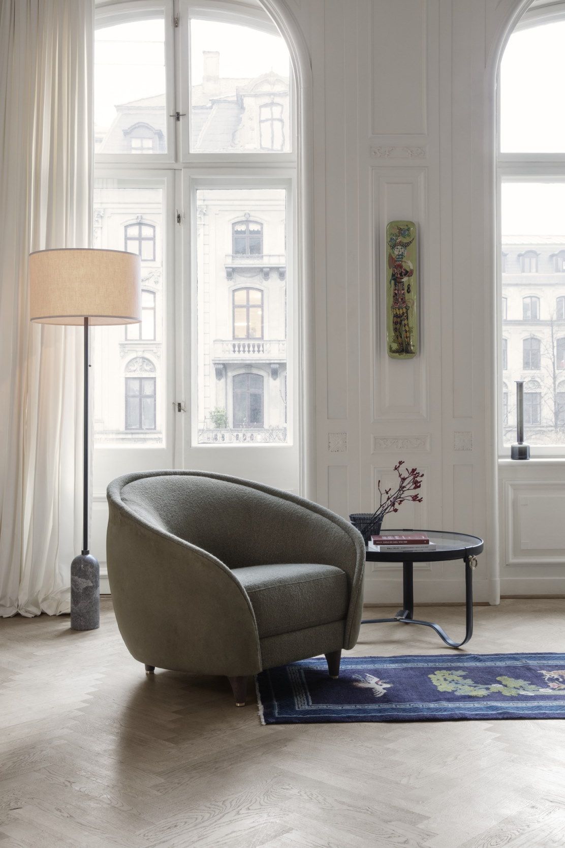 Wohnzimmer mit Gubi Couchtisch Adnet, Sessel, Stehlampe und Teppich in stilvollem Ambiente.