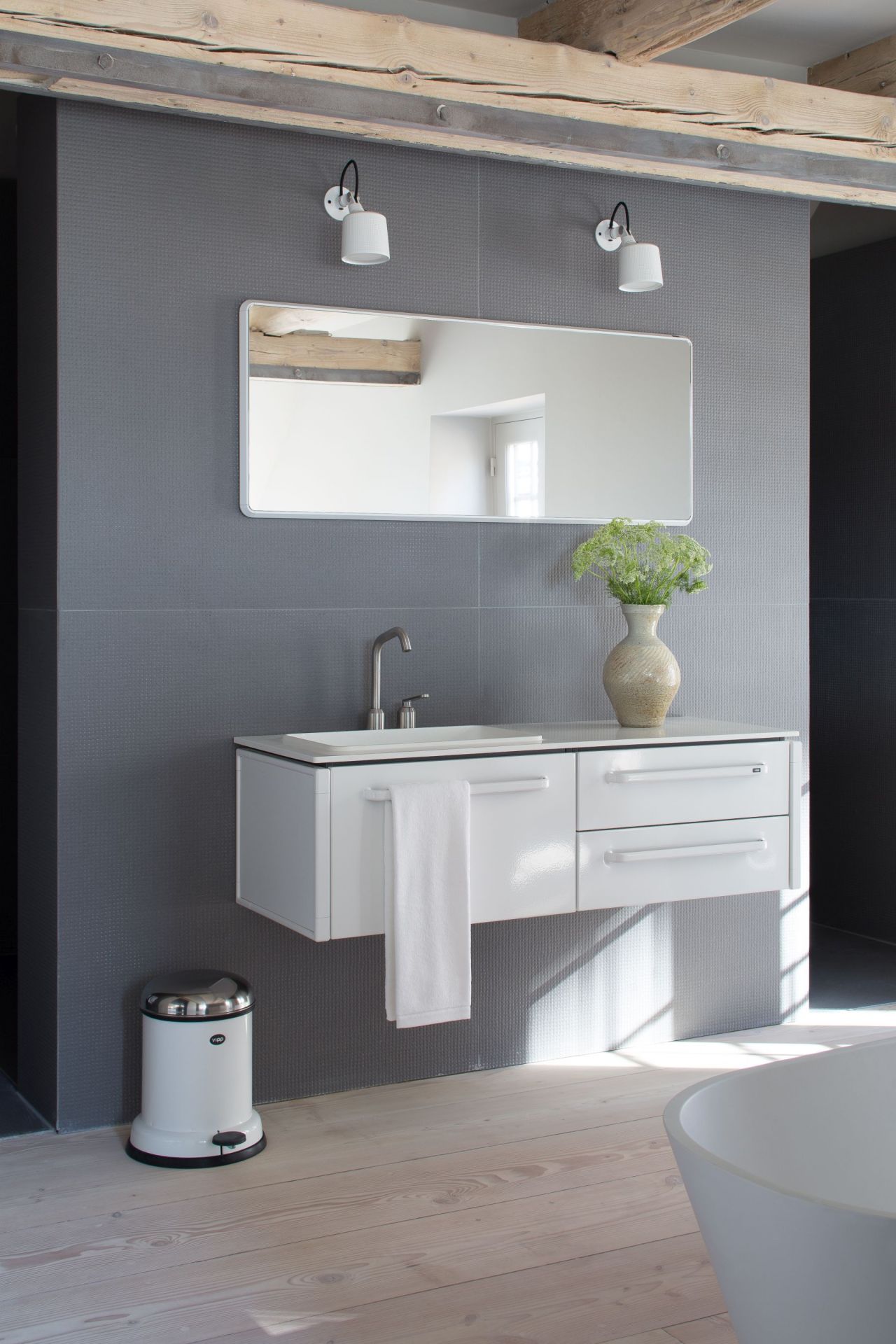 Helles Badezimmer mit weißem Vipp Wandspot, Waschbeckenunterschrank, Spiegel und passendem Treteimer für stilvolle Badgestaltung.