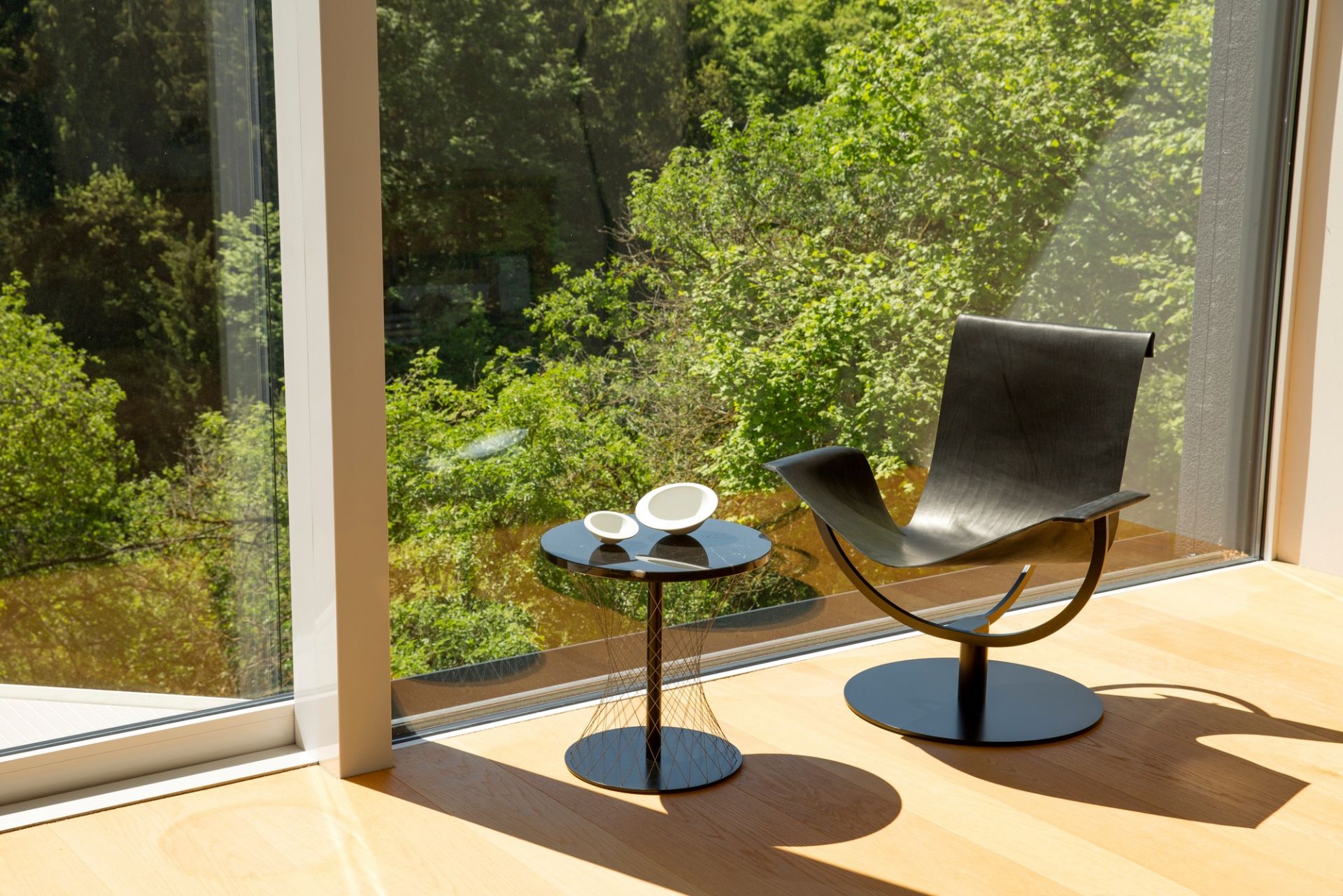 Schwarzer Network Beistelltisch Favius neben Sessel vor Fenster mit Blick ins Grüne. Moderner Beistelltisch.