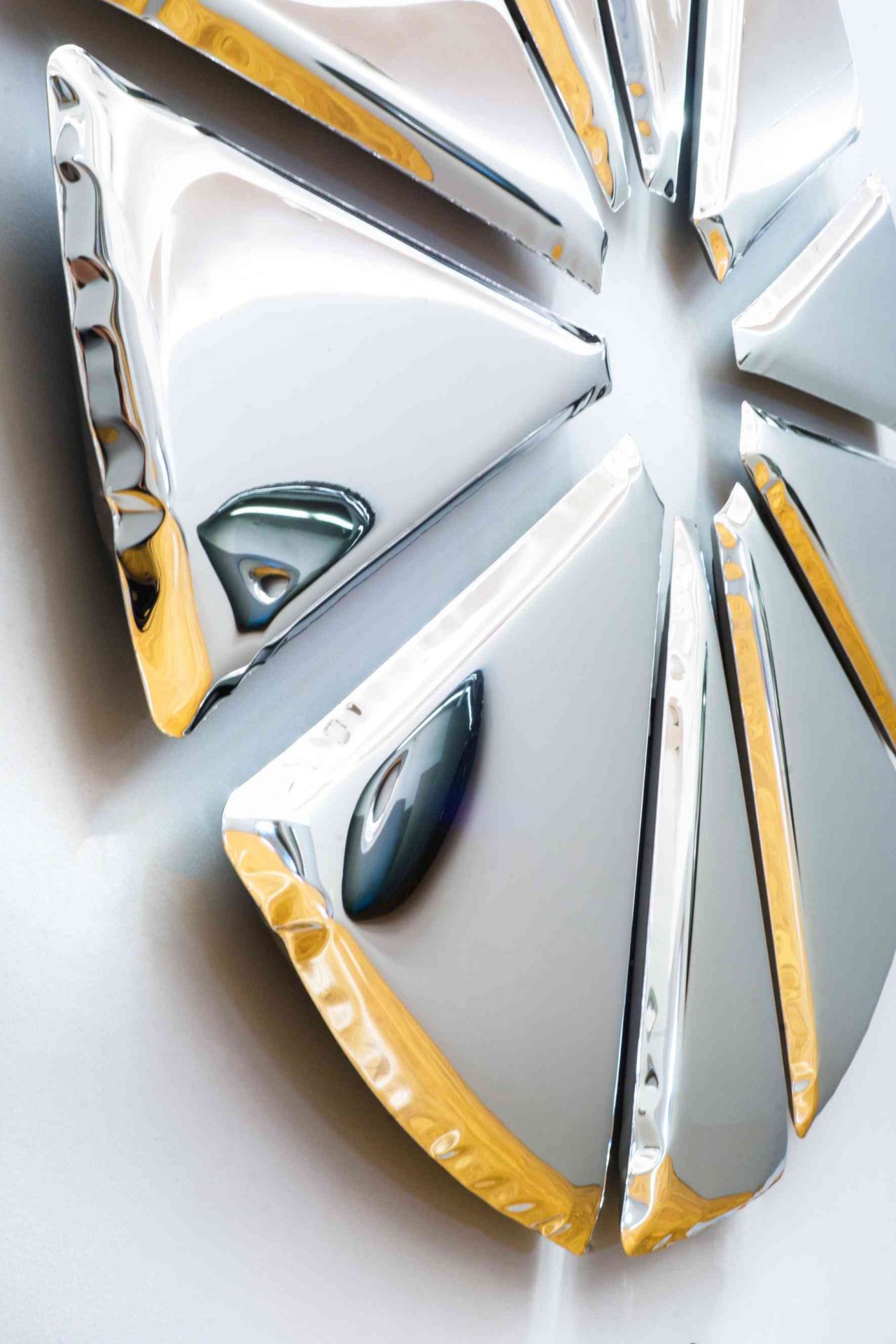 Nahaufnahme des Nucleus Spiegel Zieta, ein moderner Wandspiegel mit silbernen, dreieckigen Elementen und goldenen Akzenten.