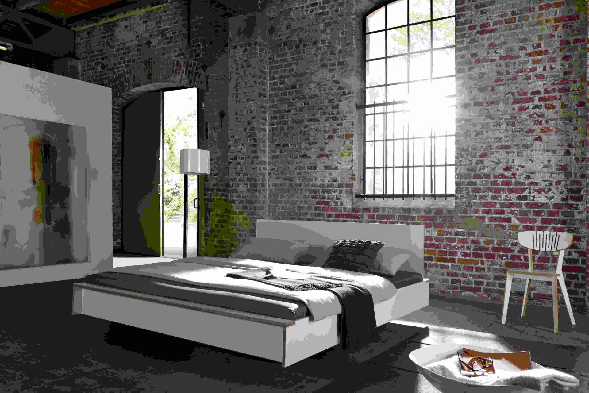 Weißes Flai Bett von Müller Möbelwerkstätten in modernem Loft mit Backsteinwand und Tageslicht.