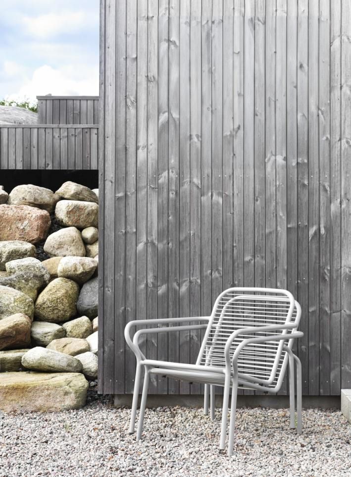 Normann Copenhagen Vig Lounge Chair Outdoor Sessel vor Holzfassade und Steinen, modernes Gartenmöbel Design.