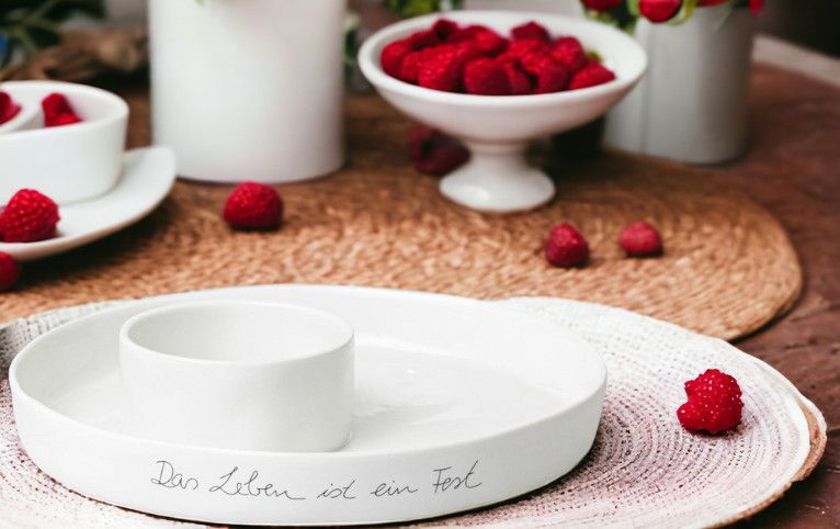 Weiße Räder Schale "Das Leben ist ein Fest" mit Dipschale und Himbeeren als Tischdeko.
