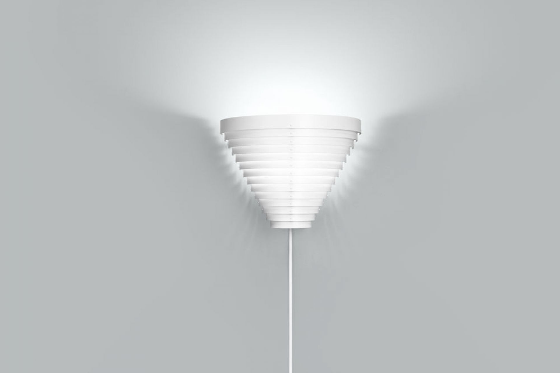 Weiße A910 Wandleuchte von Artek, Designleuchte mit Kegelform und indirektem Licht an grauer Wand.