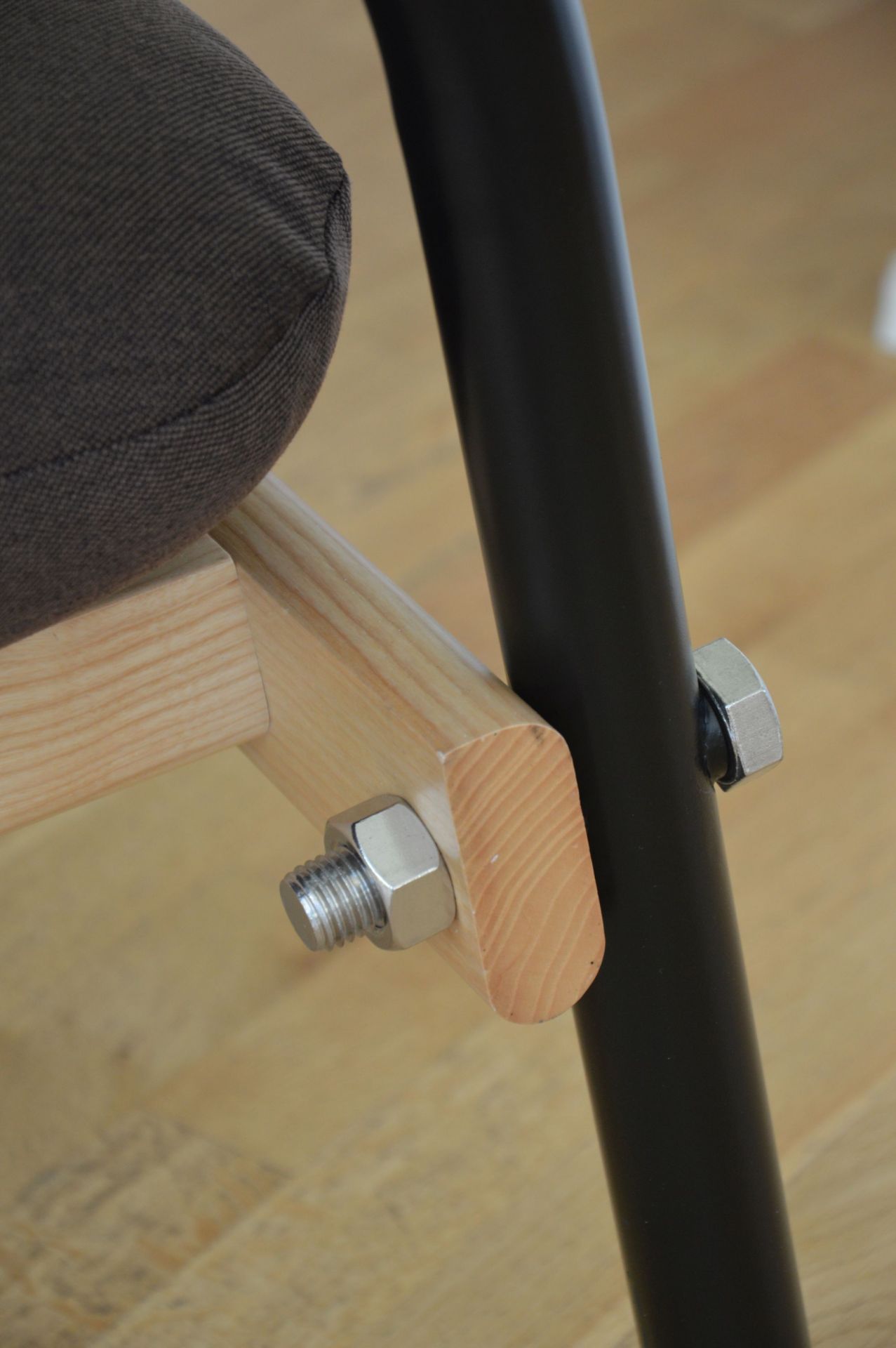 Detailaufnahme Billy Sessel: Grauer Sitz, helle Holzverbindung und schwarzes Metallgestell. Jan Kurtz Möbeldesign.