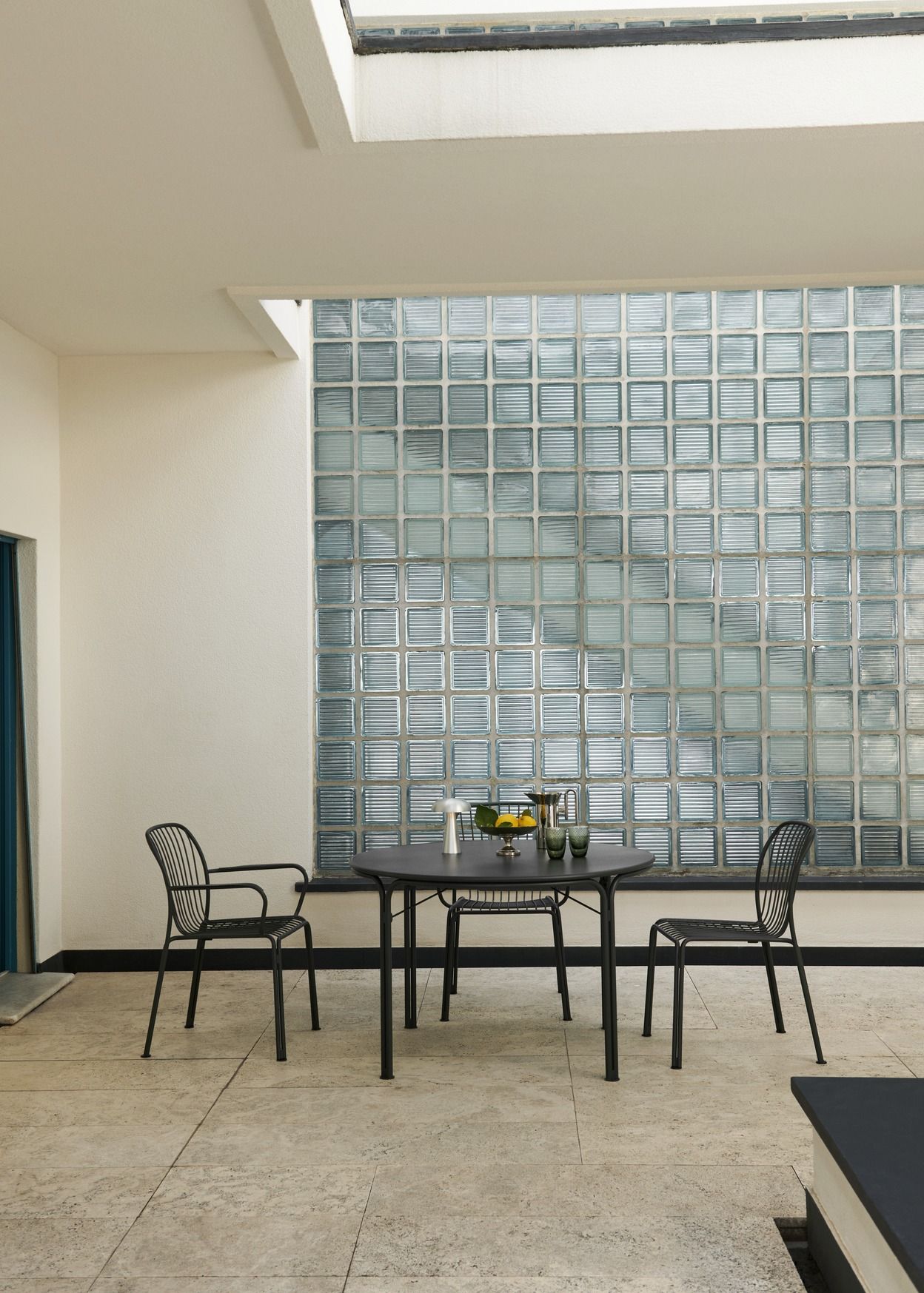 Schwarzer AndTradition Thorvald SC94 Stuhl aus Metall mit Armlehne an Esstisch im Außenbereich.