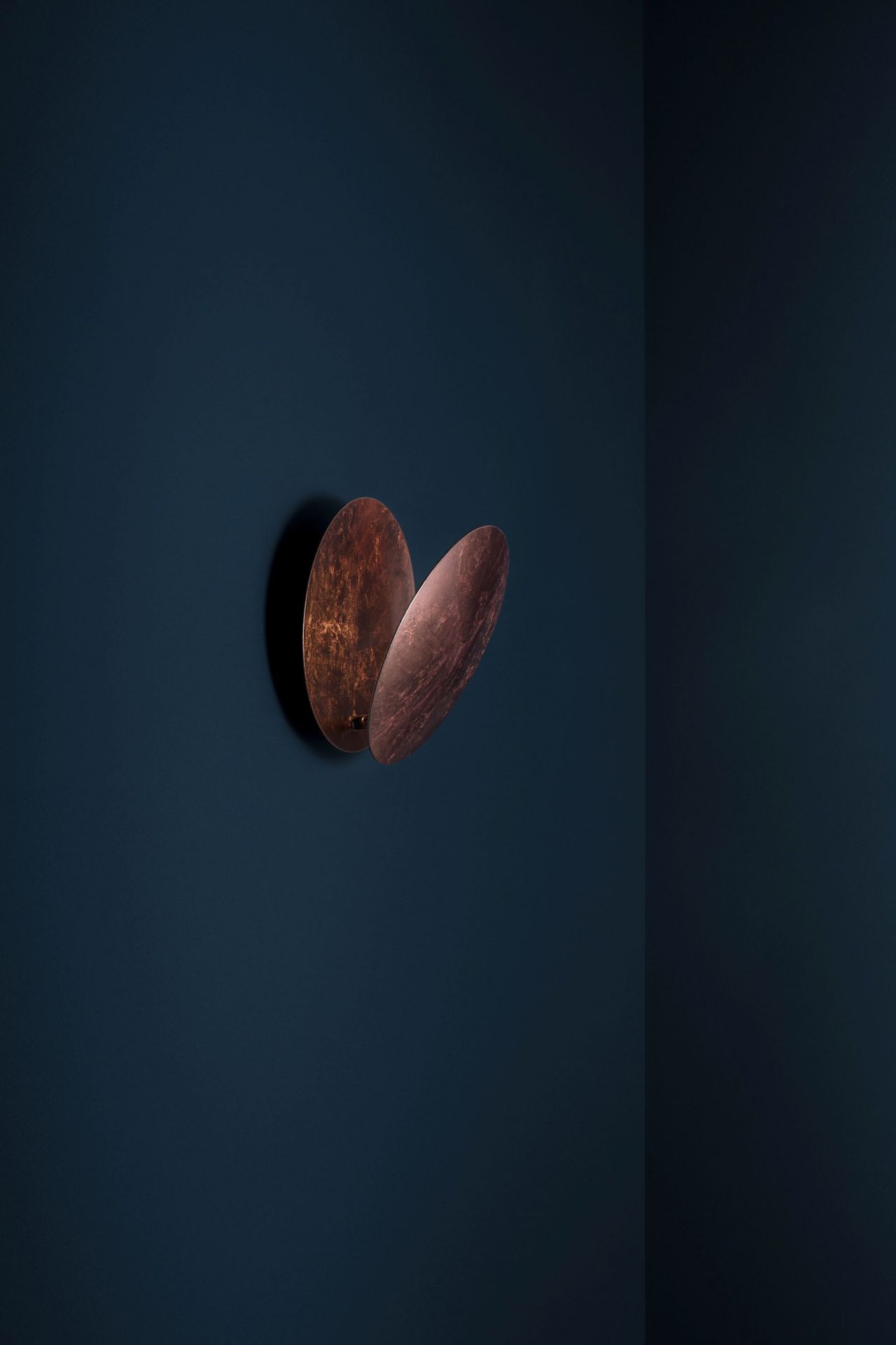 Lederam Wandleuchte von Catellani & Smith in Kupferoptik an dunkler Wand. Designleuchte für Wohnräume.