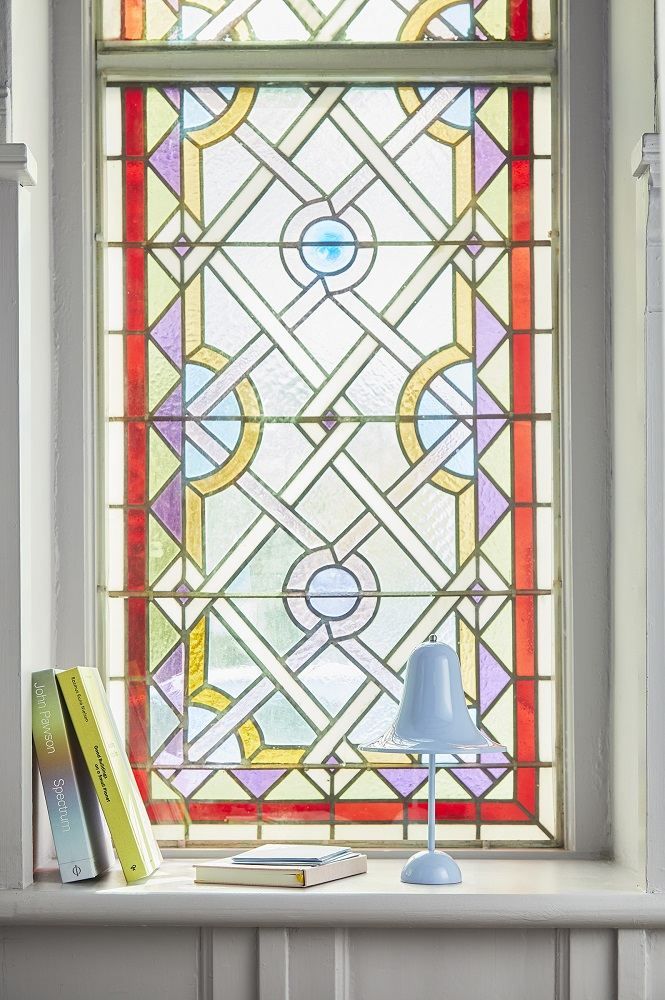 Pantop Akku Tischleuchte von Verpan in Hellblau vor buntem Fenster. Moderne portable Lampe.