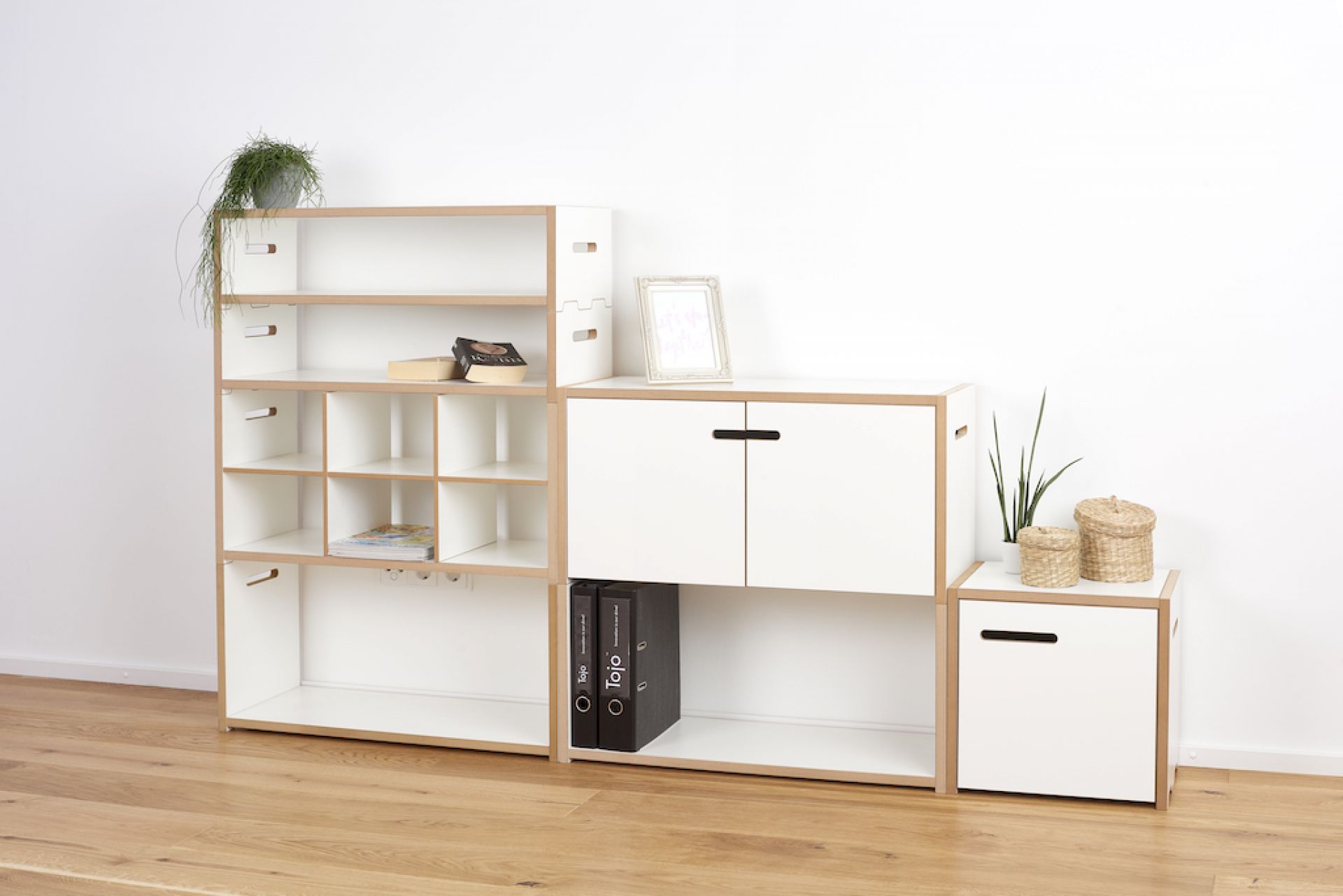 Tojo Halbstark Regalsystem: Weißes, modulares Regal mit Fächern, Schrankelementen und dekorativen Gegenständen im Wohnraum.