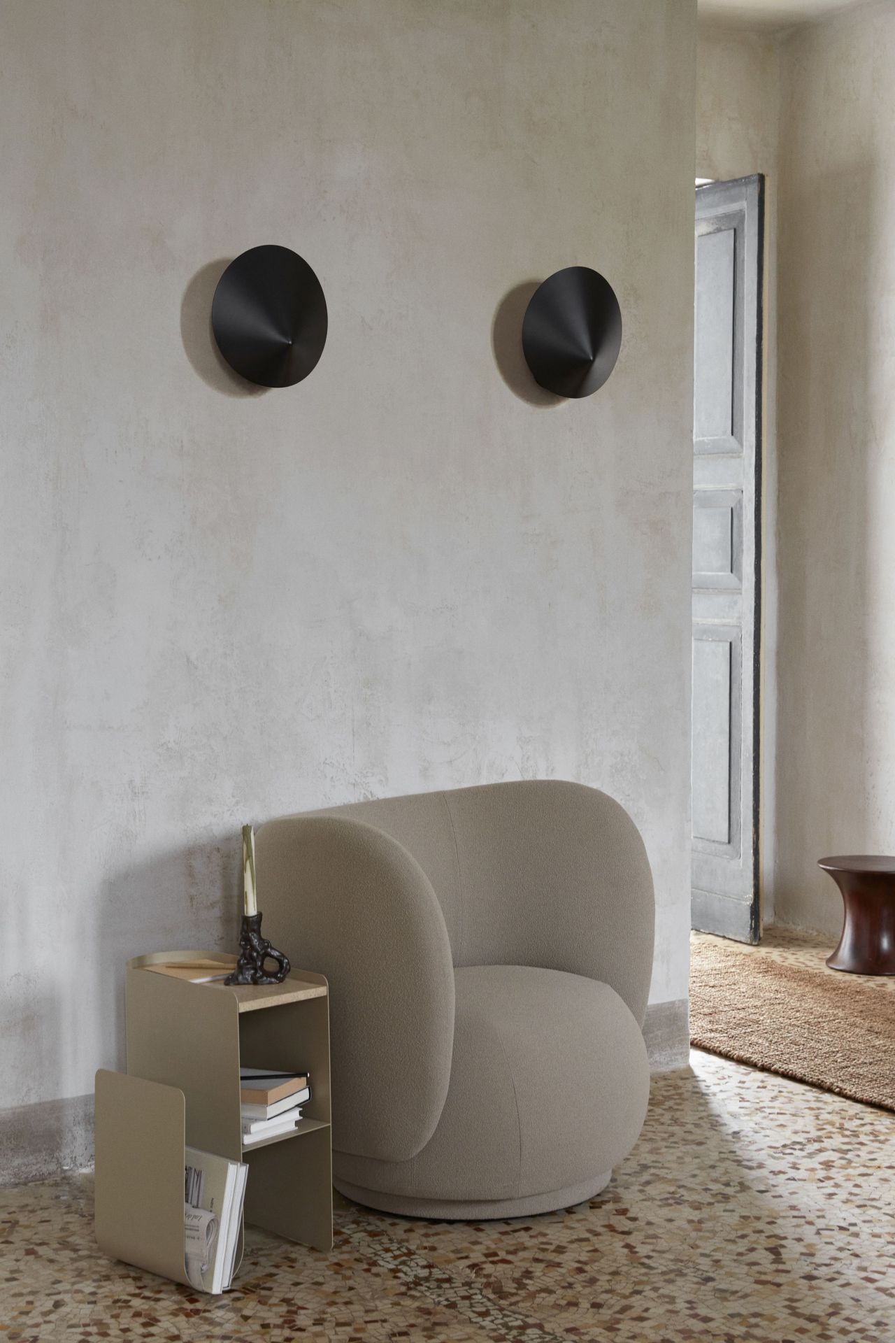 Zwei schwarze Arum Wandleuchten von Ferm Living über einem Sessel und einem Beistelltisch.