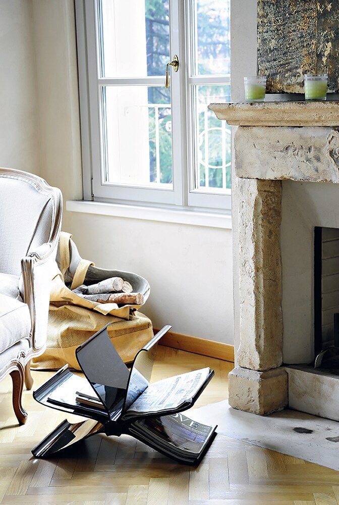 Schwarzer Kartell Zeitungsständer "Front Page" im Wohnzimmer neben Kamin und Sessel. Design Möbel für Zeitschriften.