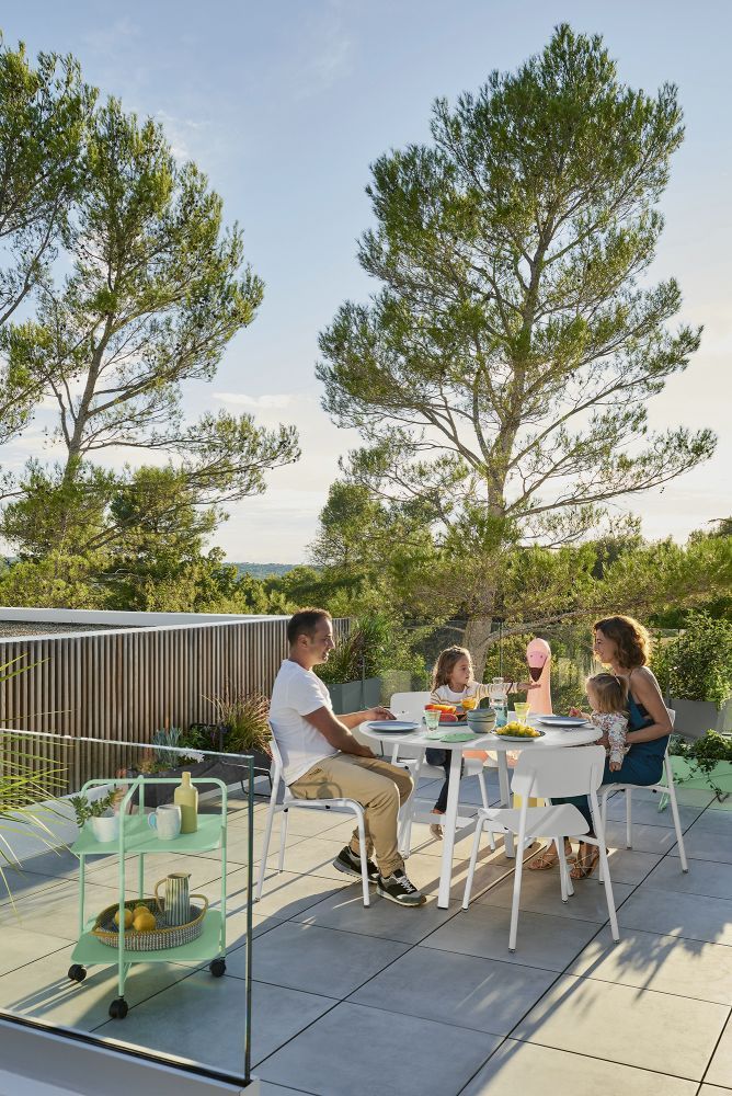 Familie sitzt am weißen SO'O Esstisch von Fermob im Freien und genießt das Essen.