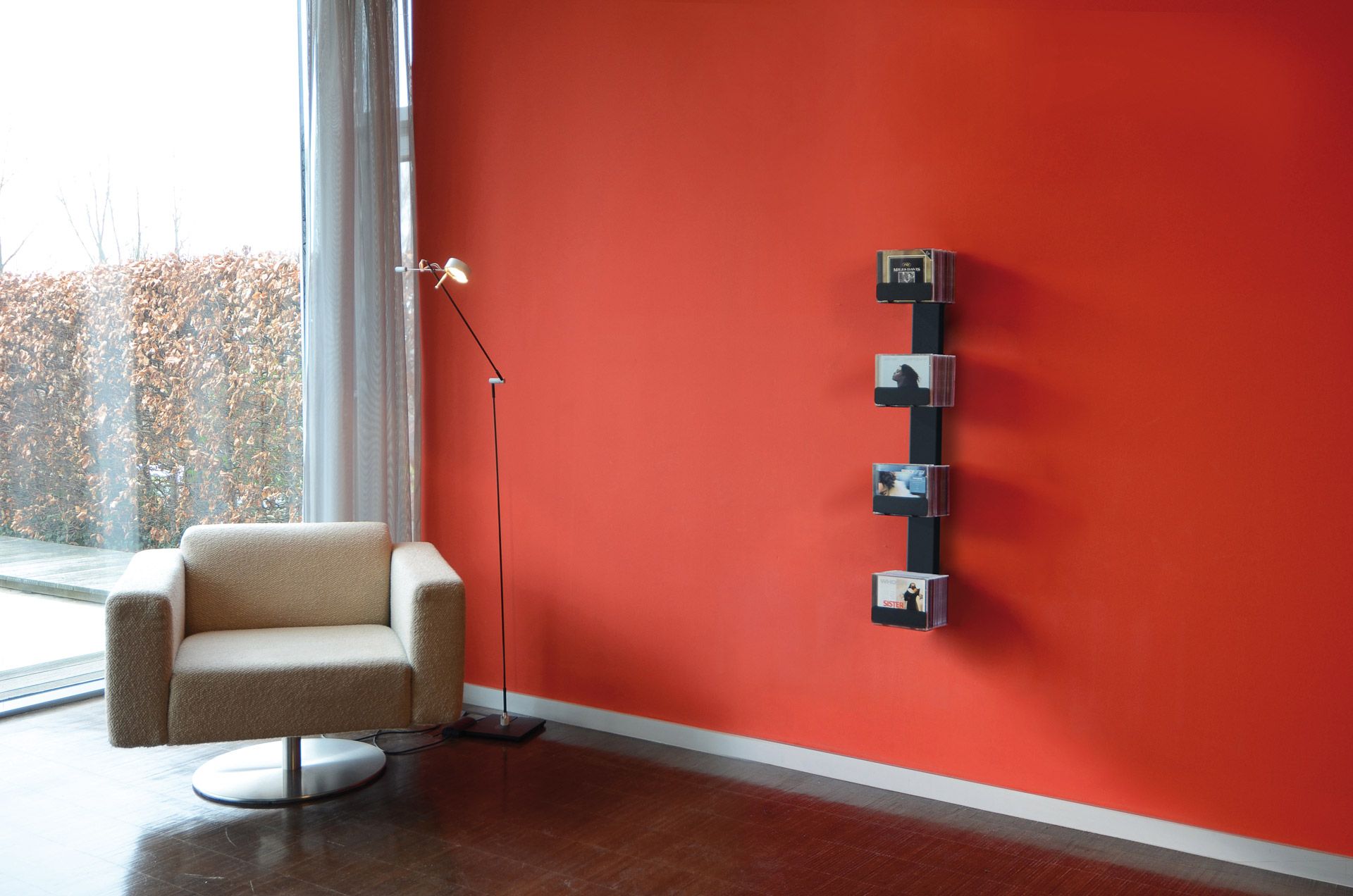 Wohnzimmer mit Sessel und CD-Baum Wandregal in Schwarz an roter Wand.