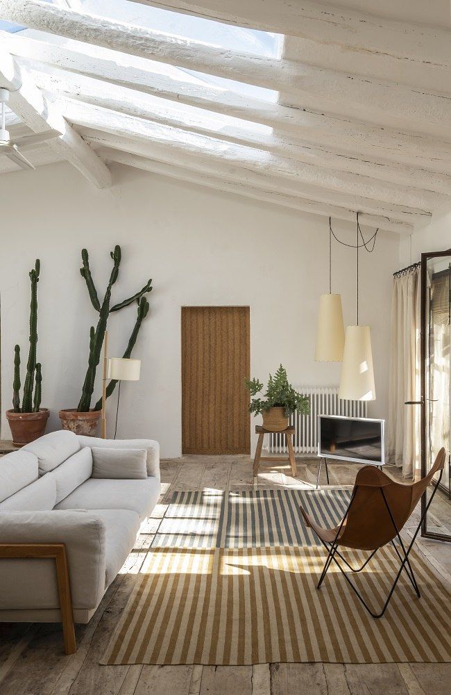 Wohnzimmer mit gestreiftem Ceras Teppich von Nanimarquina, hellem Sofa und Design-Sessel auf Holzboden.