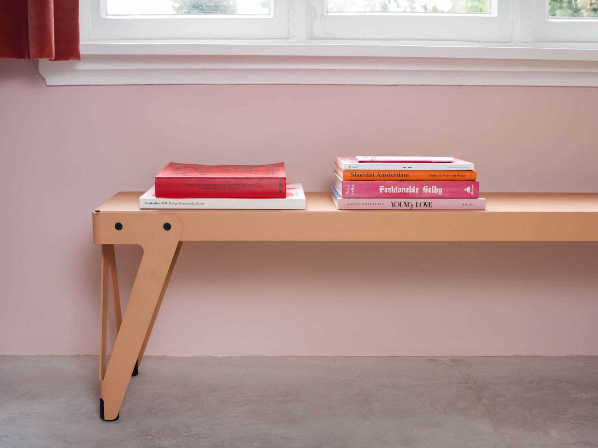 Lloyd Bank Functionals: Beige Indoor Bank mit Büchern vor rosa Wand. Sitzbank für Wohnraum.
