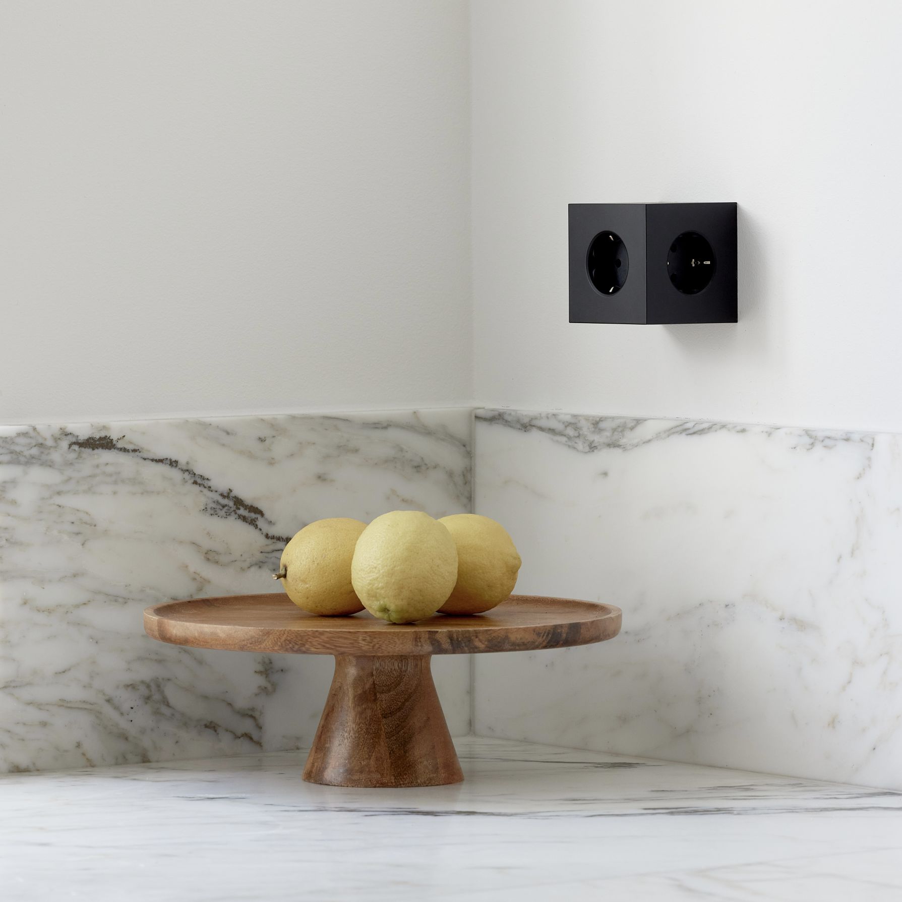 Schwarzer Avolt Square 2 Steckdosenwürfel mit USB-C an der Wand, neben Zitronen auf Holztablett.