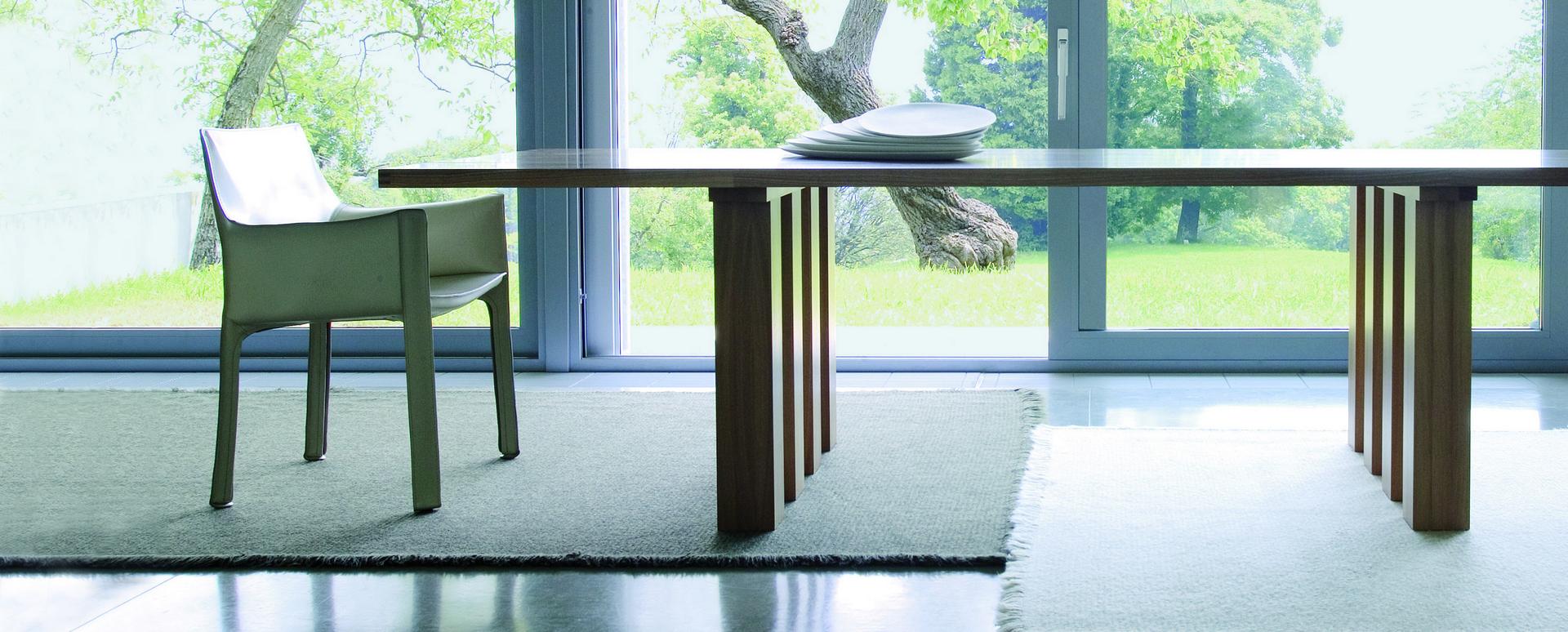 Heller Cassina Cab Armchair mit Armlehnen neben einem Holztisch vor einem Fenster.