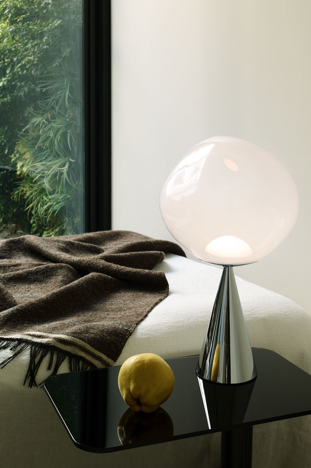 Silberne Tom Dixon Melt Cone Tischleuchte mit opalweißem Lampenschirm auf einem Nachttisch.