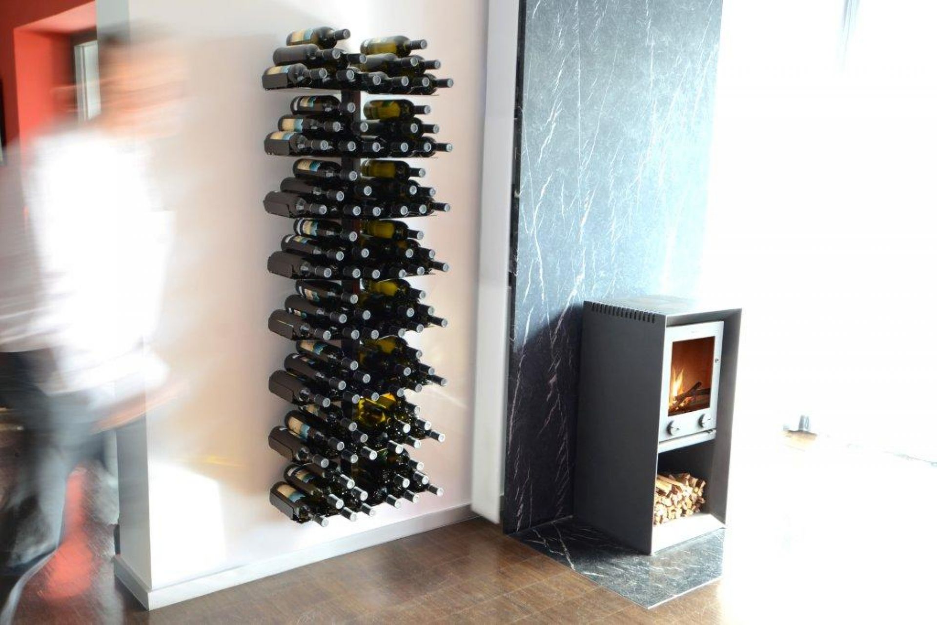 Weinregal Wine Tree Radius an einer weißen Wand, gefüllt mit Weinflaschen, neben einem Kamin.