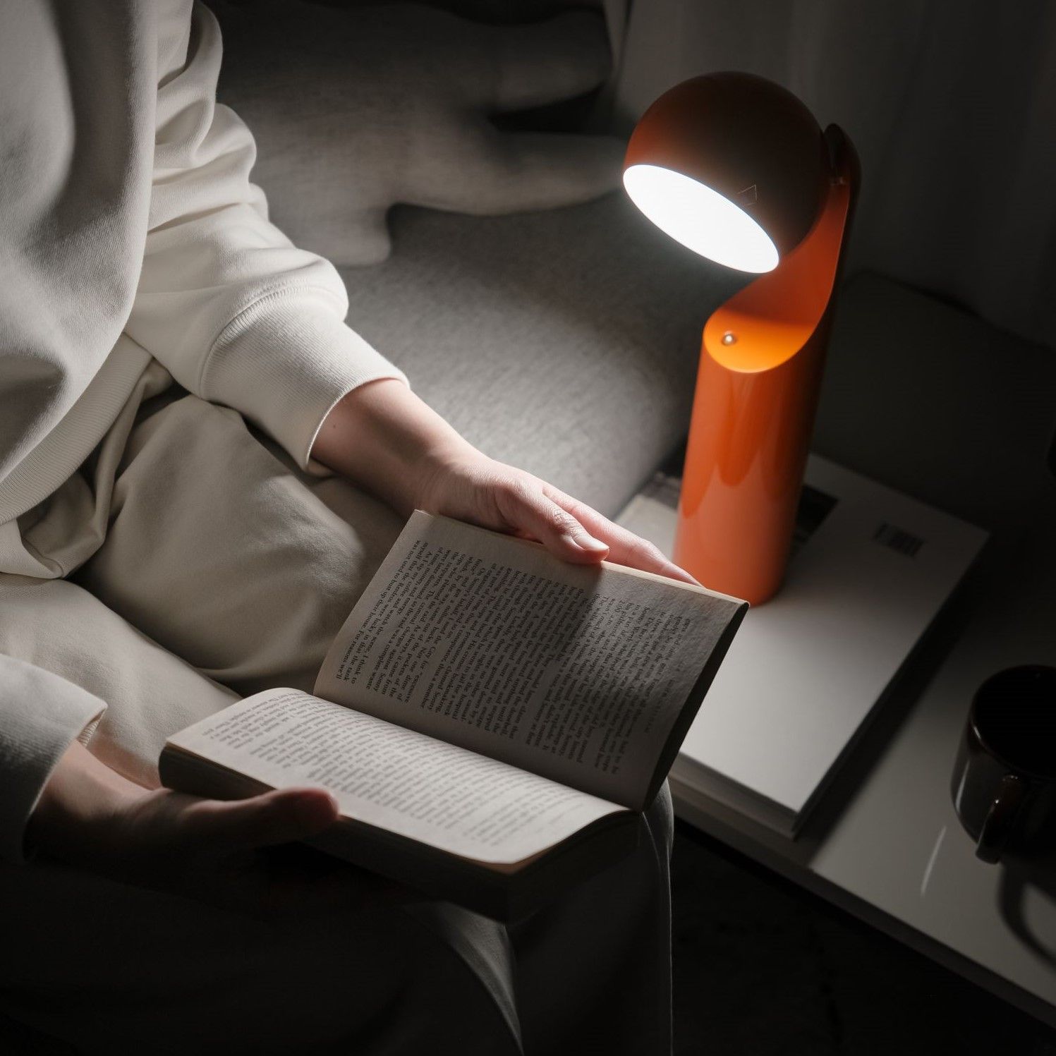 Frau liest Buch im Licht der orangefarbenen Mono Akkuleuchte / Tischleuchte.