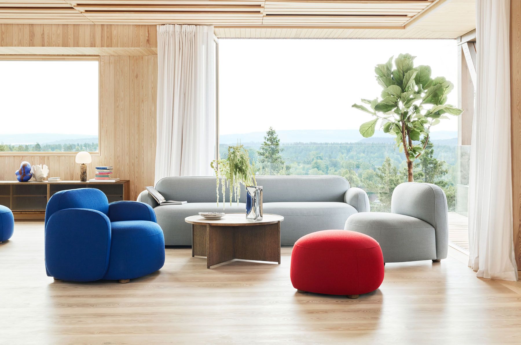 Wohnzimmer mit blauem Gem Sessel, grauem Sofa und rotem Hocker für entspanntes Wohnen.