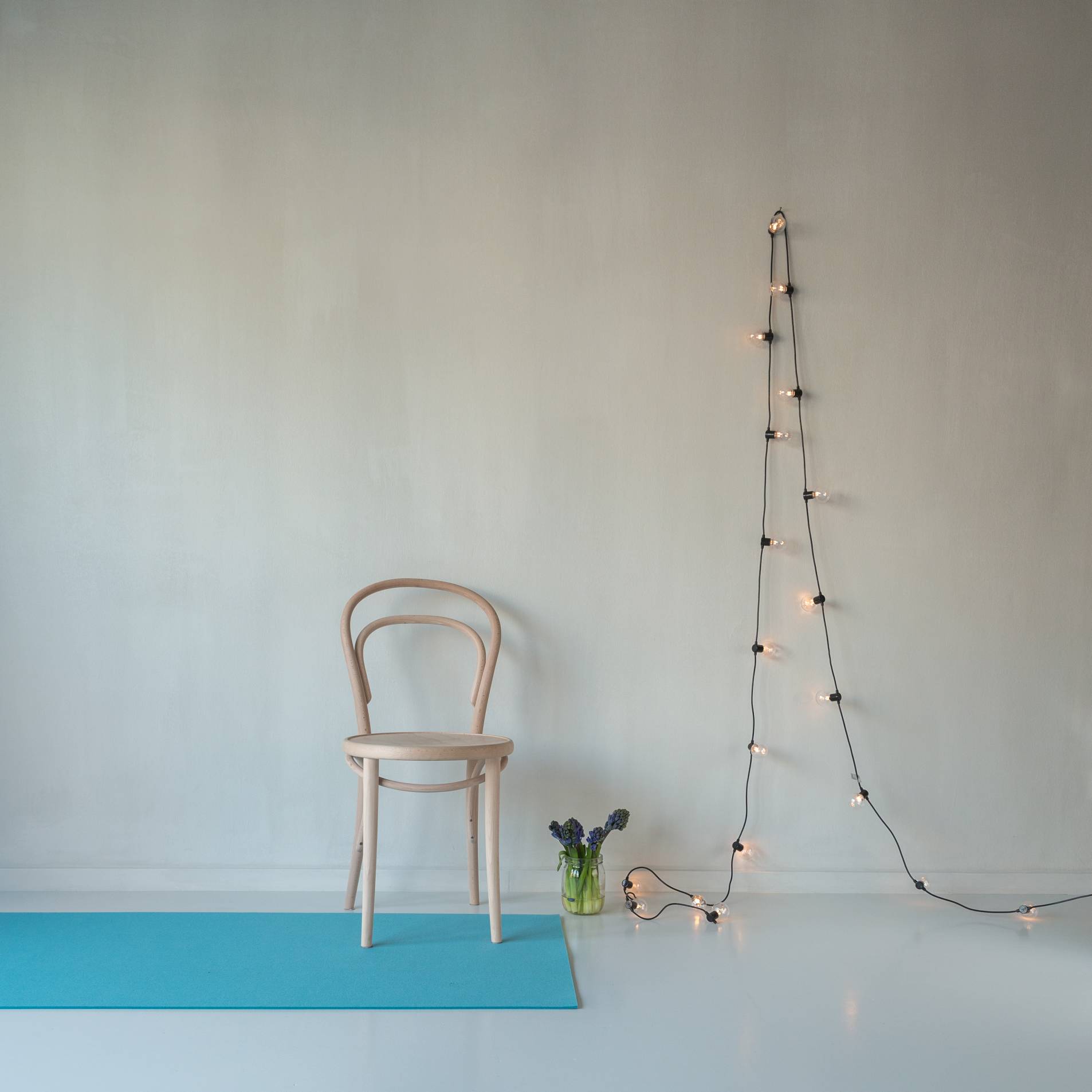 Rechteckiger, türkisblauer Hey Sign Teppich aus Filz vor einer Wand mit Stuhl und Lichterkette.