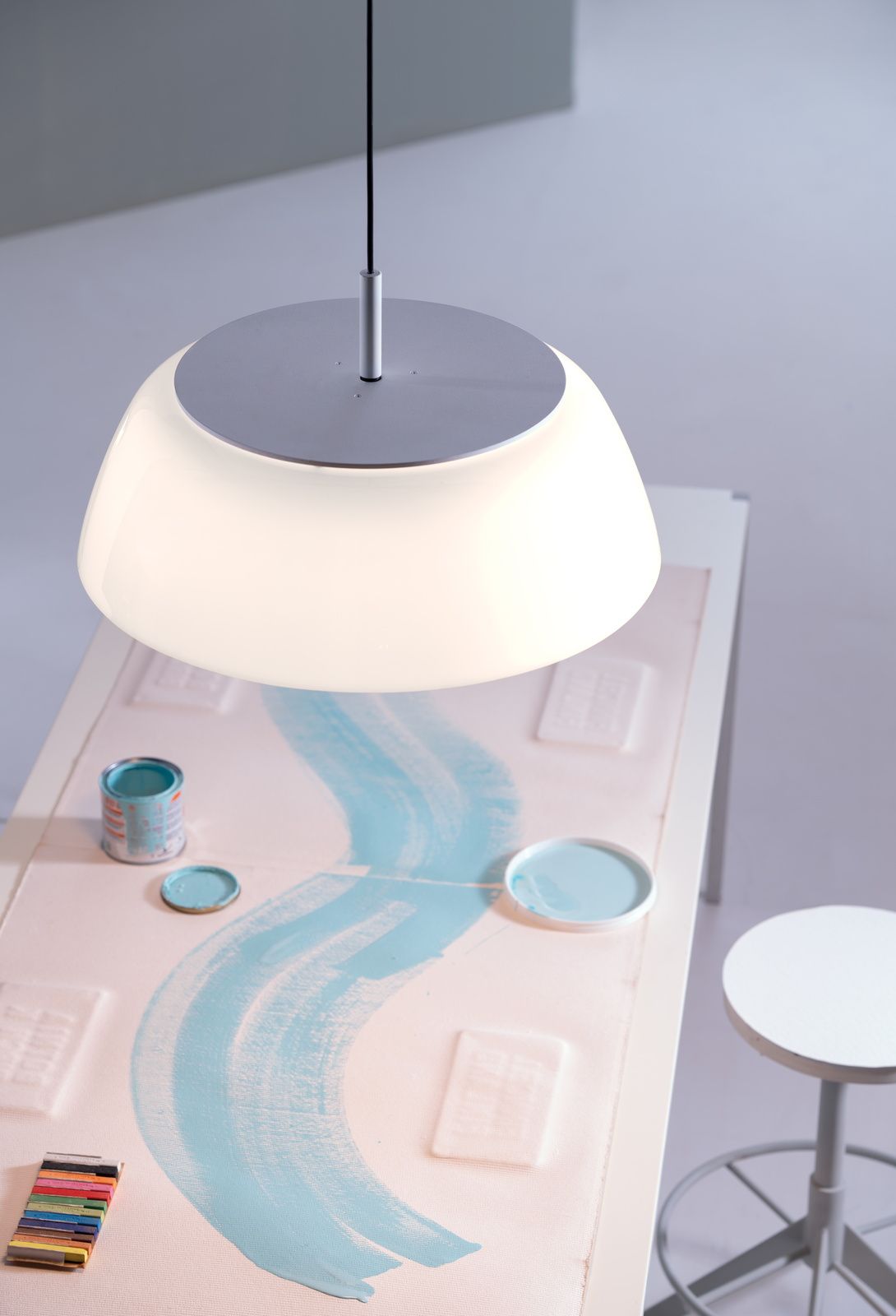 Onda Pendelleuchte von Martinelli Luce über einem Tisch mit Farbtöpfen und Pinselstrichen.