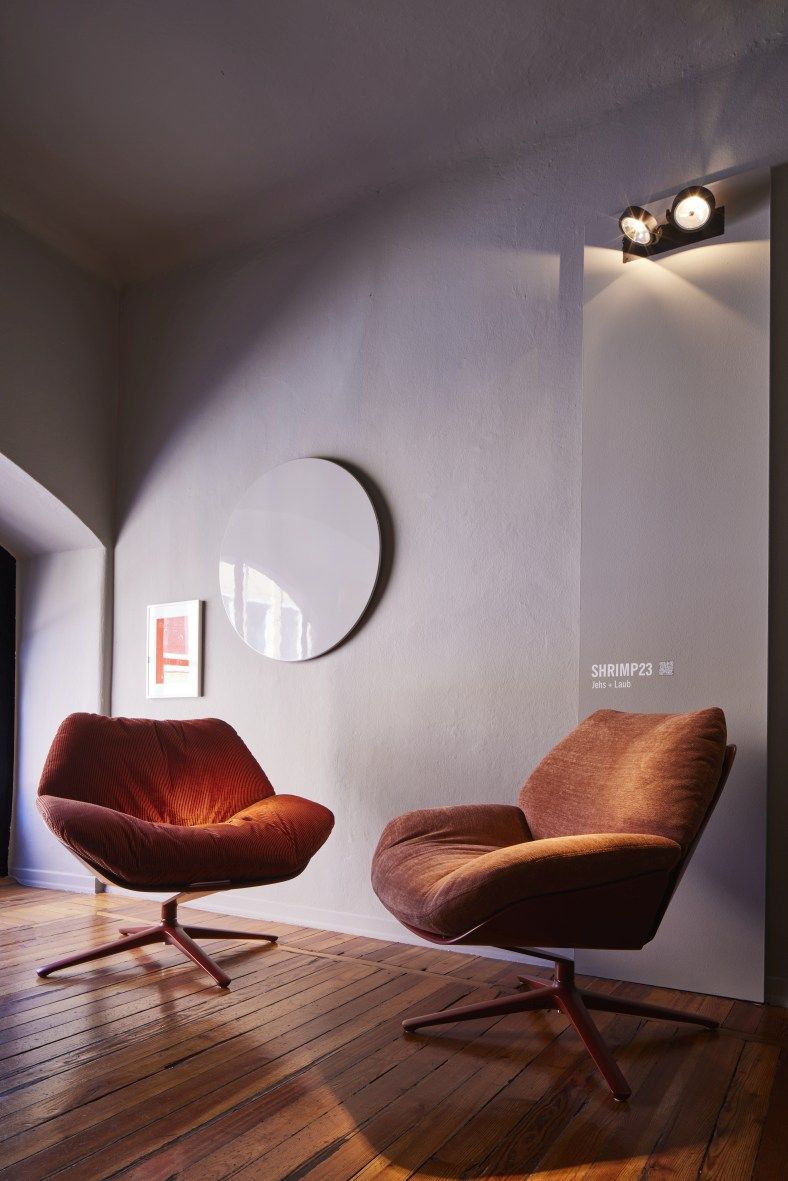 Zwei braune Shrimp Cocktailsessel mit Drehfuß auf Holzboden in einem hellen Raum.